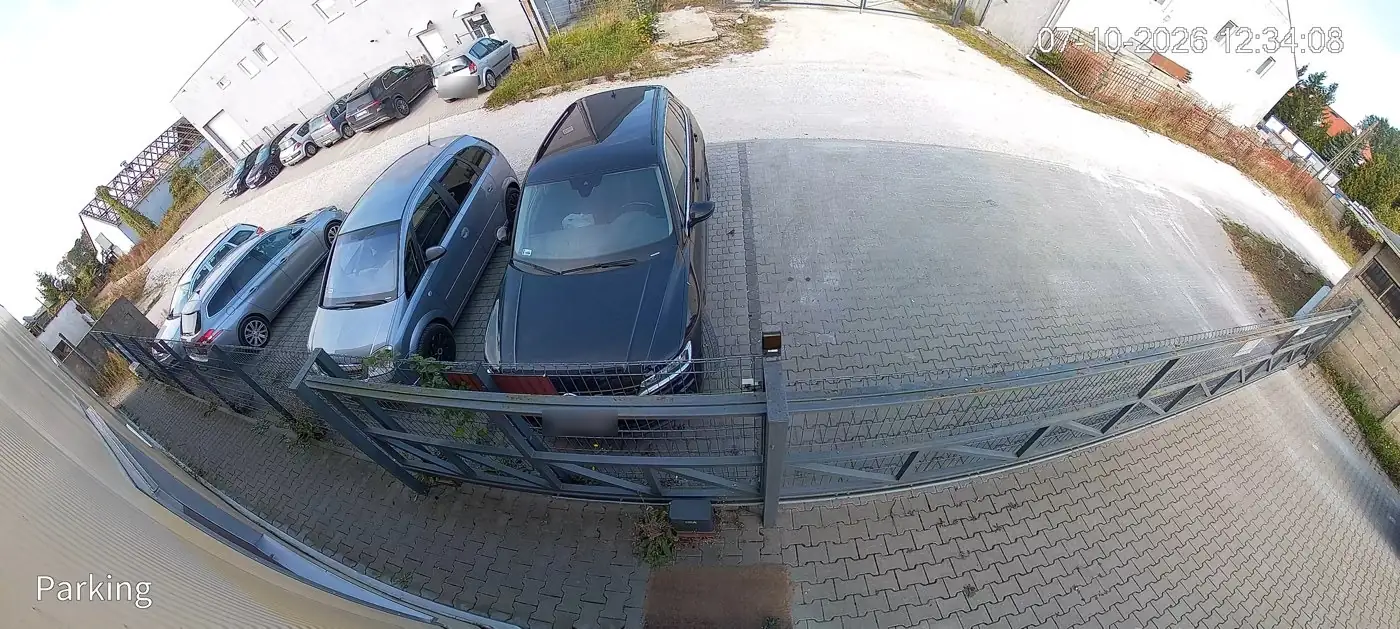 Snímek z panoramatické kamery Dahua 180° nad dlážděným parkovištěm: posuvná brána, šest zaparkovaných aut a budovy kolem dvora, říjen 2026